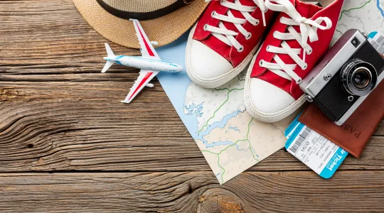 Holzdielen, darauf Sneaker, Fotokamera, Pass, Strohut, Flugtickets, kleines Flugzeit