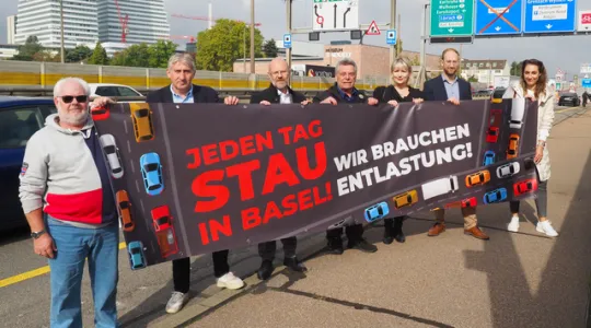 Foto der Petenten auf der Schwarzwaldbrücke (v.l.) Markus Haas, NQV Breite-Lehenmatt;  Daniel Seiler, ACS beider Basel; Lukas Ott, TCS beider Basel; Hans-Peter Ebneter, NQV Oberes  Kleinbasel; Tamara Hunziker, Gewerbeverband Basel-Stadt; Silvan Buchecker, Handelskammer beider  Basel; Birgit Kron, TCS beider Basel.  