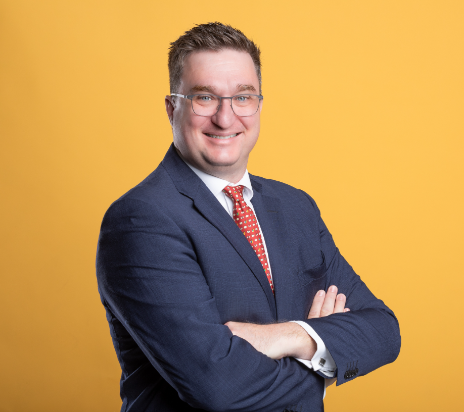 Direktor der IHK Wallis, Vincent Riesen, in einem blauen Anzug vor einer gelben Wand